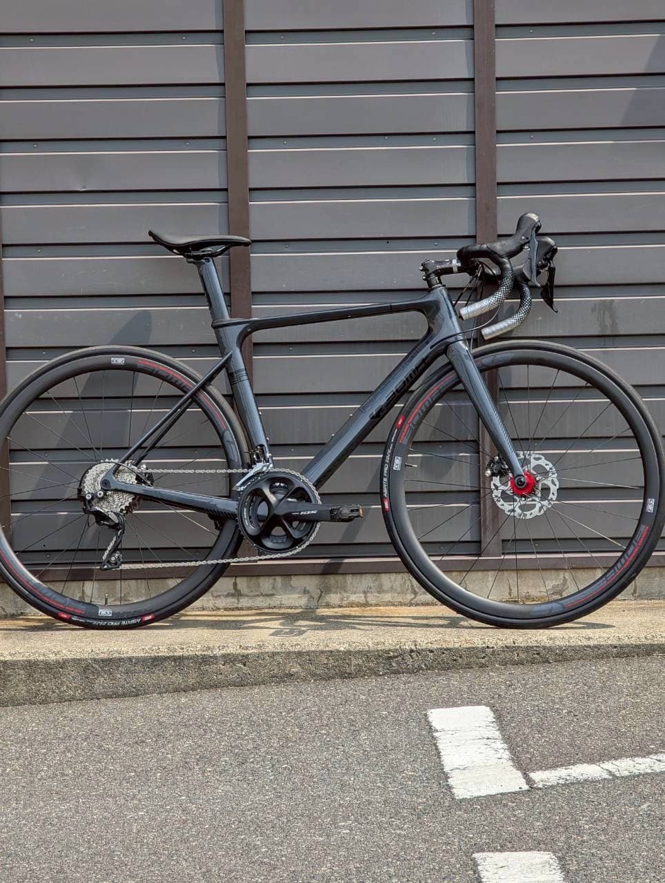 cycleZ店頭前に立てかけたBOMA RASOR Ⅱ。マットなダークグレーのカーボンフレームにディスクブレーキ、赤いハブが効いたレーシングロード